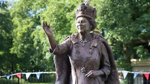 Test Valley Borough Council Close up of bronze statue of Queen Elizabeth II smiling and waving while wearing crown and royal robes