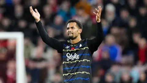 PA Media Iliman Ndiaye wears a black jersey with blue and yellow zig-zag stripes. His arms are raised in celebration after scoring a goal.